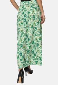 Jupe maxi fleurie verte avec un design en étages, présentant diverses nuances de fleurs vertes et violettes, fabriquée en tissu léger.