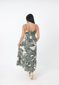 Abito lungo con spalline regolabili, caratterizzato da un motivo di foglie verdi su uno sfondo beige, e una vita arricciata con un dettaglio a fiocco.