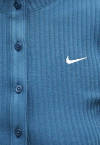 Μπλε ραβδωτό ύφασμα με τέσσερα σκούρα μπλε κουμπιά και λευκό κεντημένο λογότυπο Nike swoosh στη δεξιά πλευρά.