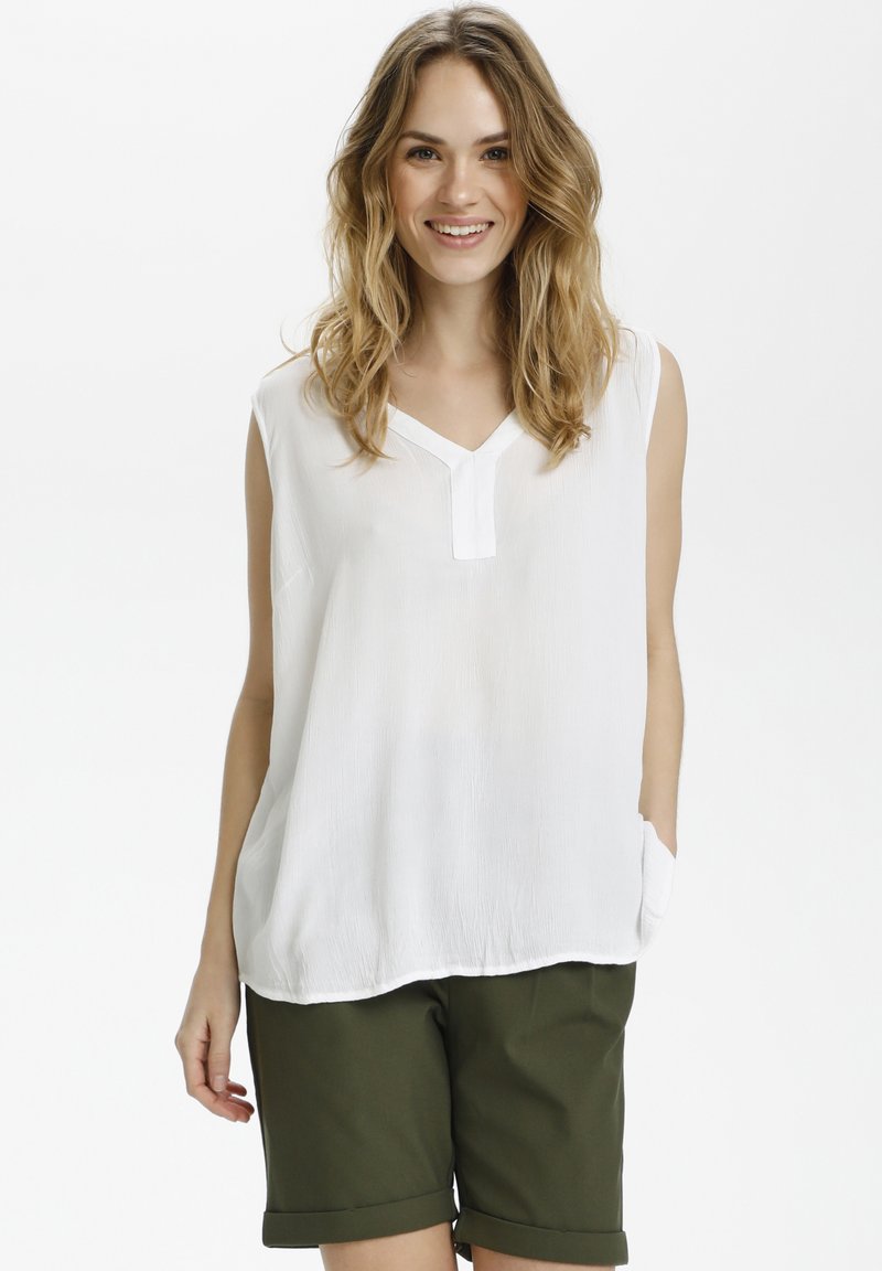Haut sans manches blanc avec un col en V et une poche avant, associé à un short vert foncé. Le haut a une finition texturée et une coupe décontractée.