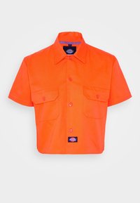 Short-sleeve shirt in bright orange fabric, featuring a pointed collar, two chest pockets, and a logo patch at the bottom.