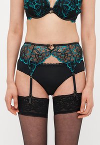 Črni komplet spodnjega perila s turkiznimi cvetličnimi čipkami. Ponaša se z visokim pasom, podvezicami in prozornimi črnimi nogavicami.