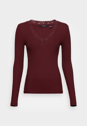 Langemouwige, getailleerde, kastanjebruine ribtop met kanten afwerking rond de V-hals, getoond op een witte achtergrond.