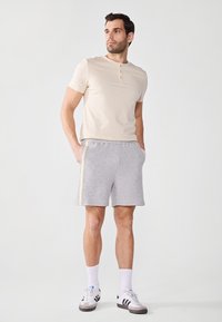 Beige short-sleeve henley shirt with three buttons, paired with gray fleece shorts featuring side stripes and white sneakers with black accents.