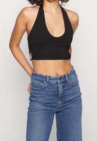 Czarny top w stylu halter z szerokim dekoltem, z wycięciami po bokach i srebrnymi akcentami, w połączeniu z niebieskimi dżinsami z wysokim stanem.