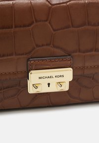Borsa in pelle marrone con un motivo testurizzato a crocifisso, dotata di una chiusura in metallo dorato e del nome del brand inciso.