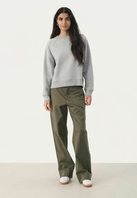 Grauer Pullover mit langen Ärmeln und geripptem Saum, kombiniert mit lockeren olivgrünen Hosen. Weiße Sneaker mit beigen Sohlen vervollständigen das Outfit.