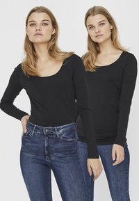 Haut noir à manches longues avec un décolleté en bateau, fabriqué dans un tissu doux. Porté avec un jean en denim bleu à taille haute et à cinq poches traditionnelles.