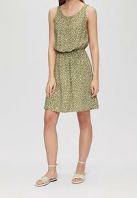 Grön klänning med lös passform, vita prickar, rund halsringning och dragsko i midjan. Matchas med beiga sandaler med remmar.