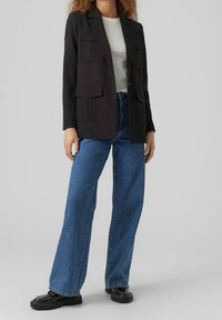 Svart blazer med stora framfickor, kombinerad med högmidjade blå jeans och svarta skor. Outfiten har en texturerad, ribbad vit topp.