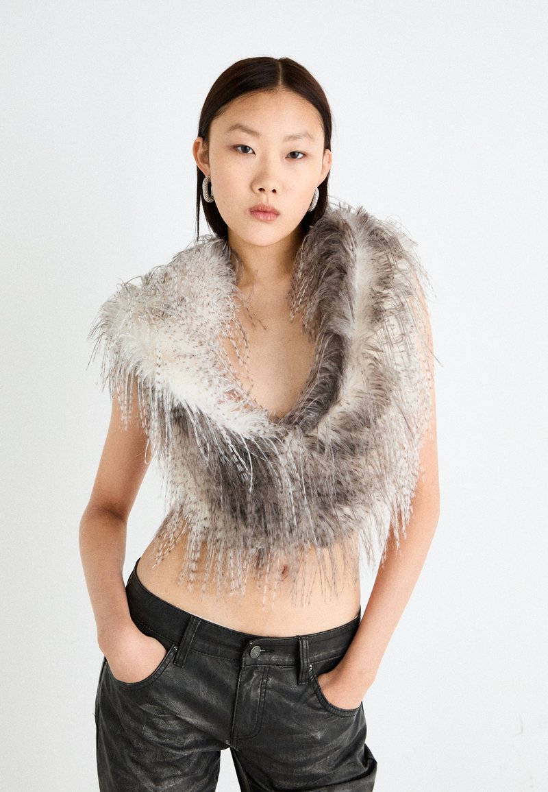 Faux päls croppad scarf i gradientnyanser av grått och vitt, med långa, fjäderlika fransdetaljer. Bärs över bar hud och svarta läderbyxor.