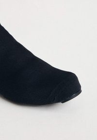 Črne nogavice z gladko teksturo, z zaobljenim prstom in subtilnim rebrastim dizajnom blizu manšete, primerne za sproščeno nošenje.