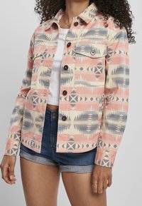 Patterned denim jacket featuring pink, blue, and beige geometric designs, with two front pockets, button closures, and a slightly textured finish.