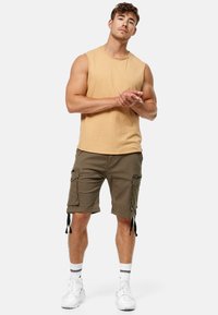 Chemise sans manches jaune clair associée à un short cargo vert olive avec des poches et des liens ajustables, complétée par des baskets blanches.