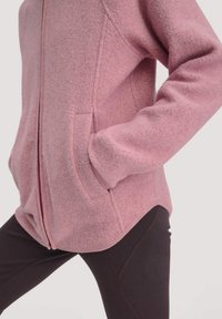 Giacca in pile rosa con chiusura a zip, tasche laterali e superficie testurizzata. Abbinate a leggins scuri con un design di cuciture a contrasto.