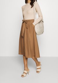 Beige texturovaný dlouhý rukáv top spárovaný s hnědou midi sukní s páskem v pase a knoflíky, doplněný béžovými sandály na podpatku a kabelkou.