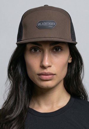 Woman with long dark hair wearing a brown and black BLACKSKIES Pro cap and a black shirt, facing forward with neutral expression.