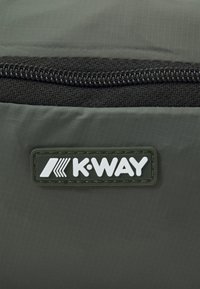 Pocchetto di tessuto grigio con superficie testurizzata, dotato di una zip nera e di un distintivo rettangolare verde con la scritta "K-WAY" in lettere bianche.