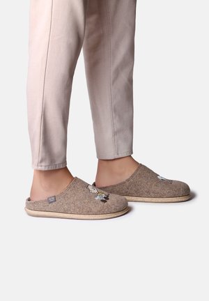 Bruna tofflor i filt med platta sulor, prydda med broderade tecknade figurer på framsidan. Kombineras med ljusbeige, slim-fit byxor.