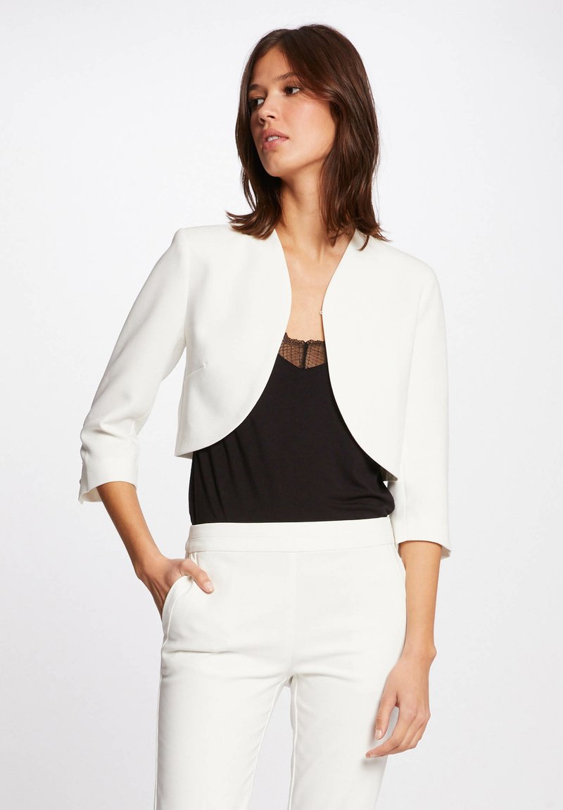 Weißer, verkürzter Blazer mit Dreiviertelärmeln und ohne Verschluss, getragen über einem schwarzen Tanktop, das ein schlankes, strukturiertes Design betont.