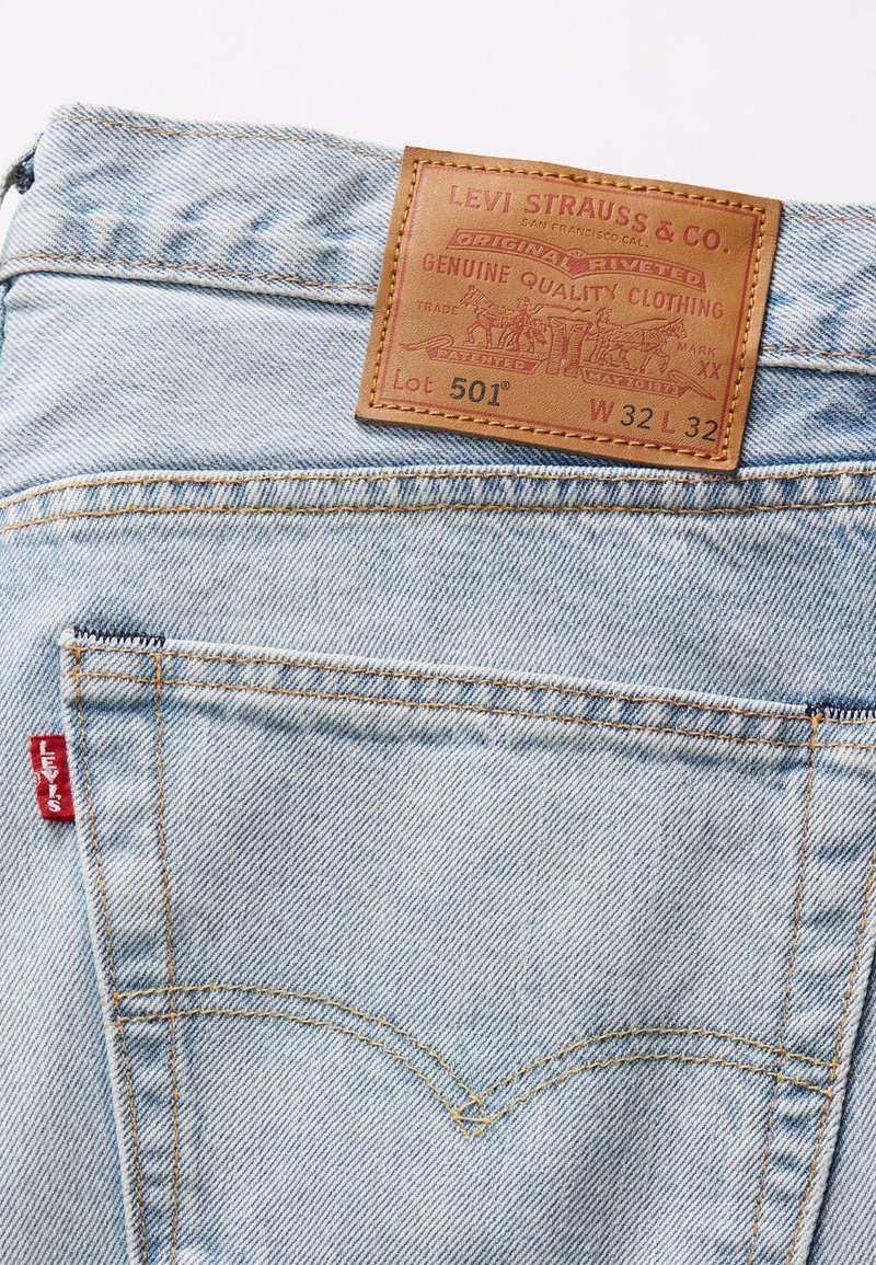 Lichtblauwe denim jeans met een leren label "LEVI STRAUSS & CO." en rode tabdetails. Bevat zichtbare stiksels en gebogen achterzakken.