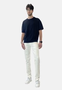Camiseta negra de algodón, jeans ajustados blancos y zapatillas blancas. Gafas, reloj plateado y un pequeño collar acentúan el look.