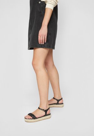 Mustat kudotut nahkajalkineet, joissa on espadrille-tyylinen juuttipohja, säätöremmi nilkassa ja litteä alusta.