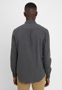 Camisa de cuadros en blanco y negro con mangas largas, cuello estándar y dobladillo curvado. Presenta puños abotonados y un corte relajado.