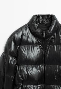 Giacca imbottita nera con collo alto, finitura lucida e design trapuntato orizzontale. Chiusura frontale con cerniera e texture imbottita elegante.