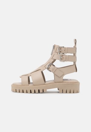 Beige sandaaltjes met straps en een dikke plateauzool, voorzien van meerdere verstelbare gespen en een zijrits. Duurzaam, gestructureerd materiaal.