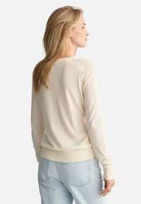 Maglione beige chiaro con polsini e orlo a costine, caratterizzato da una consistenza liscia e un semplice design a girocollo, abbinato a jeans azzurri.