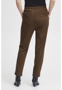 Bruine, gestreepte broek met een elastische tailleband en achterzakken, slim fit en taperend naar de enkel, gecombineerd met zwarte hakken.