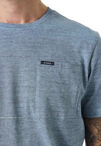 Camiseta de rayas azules con cuello redondo, mangas cortas y un bolsillo en el pecho que presenta una etiqueta oscura. Textura de tela suave y ligera.