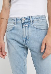 Světle modré džíny z denimu s klasickým pětipocket designem, zapínáním na knoflík a jemným odřením. Texturovaná látka s mírným elastickým efektem.