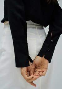 Camisa negra de manga larga con detalles en los puños y botones, combinada con pantalones blancos de tiro alto que tienen bolsillos traseros y una textura suave.