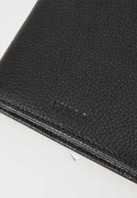 Black leather wallet featuring a textured surface and embossed "HUGO" logo. Minimalist design with clean edges.