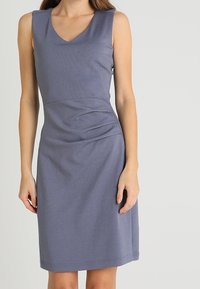 Vestido sin mangas en gris oscuro, con escote en V, detalles fruncidos en la cintura y un Bajo a la altura de la rodilla. Textura suave.