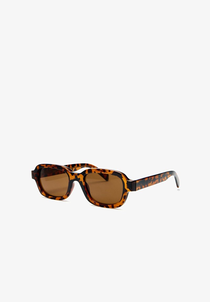 Lunettes de soleil rectangulaires avec de grosses montures écaille de tortue marron et des verres teintés marron sur fond blanc.