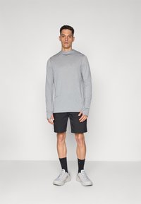 Grå hettegenser med lange ermer, kombinert med svarte shorts, grå joggesko og svarte sokker. Glatt stoff, avslappet passform, enkelt design.