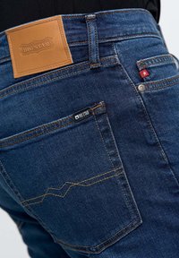 Jeans de mezclilla azul oscuro con una etiqueta de cuero que dice "BIG STAR" en la cintura, con costuras en contraste y un diseño decorativo en el bolsillo trasero.