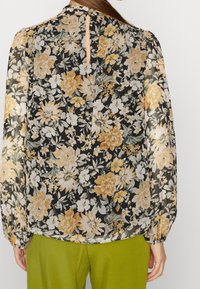 Blommig blus i svart chiffong med gula och vita blommor, långa ärmar med elastiska manschetter och ett nyckelhål i ryggen.