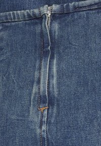 Tmavě modrý denimový materiál s uzávěrem na zip, viditelným šitím v béžové barvě a nenápadným blednutím v oblasti zipu.