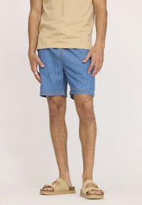 Shorts en denim bleu clair, avec une coupe droite, des ourlets retroussés et un design classique à cinq poches, associés à des sandales à glissière beige.