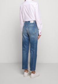 Ljusblå denimjeans med höga midja, rak benpassform och synliga bakfickor. Tillsammans med en vit skjorta med krage och vita sneakers.