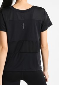 Camiseta deportiva negra con paneles de malla, mangas cortas, cuello redondo y una fila vertical de puntos reflectantes en la parte posterior.