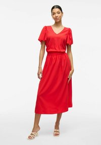 Robe midi rouge avec des manches courtes bouffantes, décolleté en V et taille élastique. Fabriquée en tissu lisse, elle présente une silhouette fluide et une coupe décontractée.