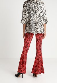 Uppflutna leggings i röd med svart leopardtryck, kombinerat med en topp i svart och vitt leopardtryck. Texturen verkar mjuk och slät.