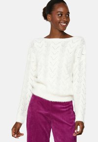Witte gebreide sweater met een zigzagpatroon, wijde halslijn en geribbelde manchetten, gecombineerd met paarse corduroy broeken.