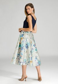 Jupe midi florale en crème avec des motifs bleus et orange ; assortie à un haut sans manches bleu marine. Elle présente une texture lisse et un design évasé.