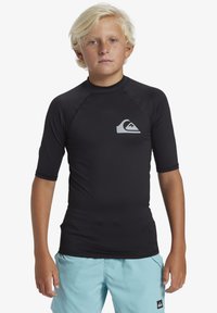 T-shirt de surf noir à manches courtes en tissu extensible, avec un logo en forme de vague gris sur la poitrine gauche et des détails de coutures plates.